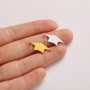 Macro view of gold and silver stainless steel graduation cap charms held on a finger