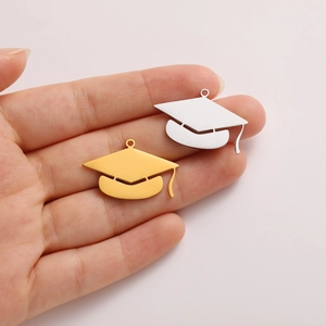 Detail of gold and silver graduation cap charms held in hand for size comparison
