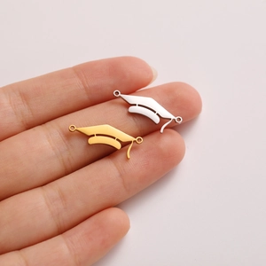 Macro detail of graduation cap pendants in gold and silver steel on a fingertip