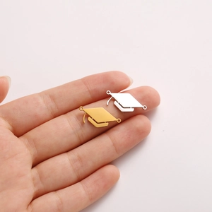Detailed view of graduation cap charms in gold and silver held to show size for DIY jewelry
