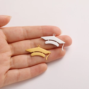 Close-up of gold and silver graduation cap charms held in hand for size perspective