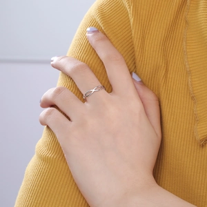 Detailopname van een zilveren infinity ring aan vinger met gele gebreide achtergrond