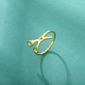 Vista de detalle de un anillo dorado en forma de tijera sobre fondo verde suave