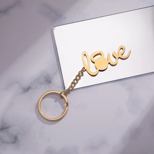 Polished gold stainless steel Love keychain with kettlebell gym charm on marble background