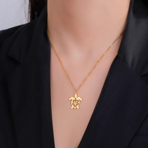 Golden hollow turtle pendant necklace with floral patterns worn on a black blazer
