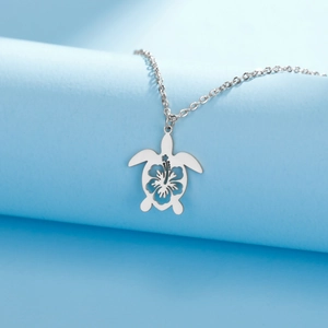Detail of silver turtle pendant with hibiscus pattern on light blue roll paper