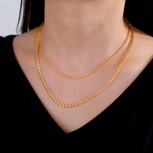 Detail of layered gold cuban link chain necklace on model neck with black V-neck top
