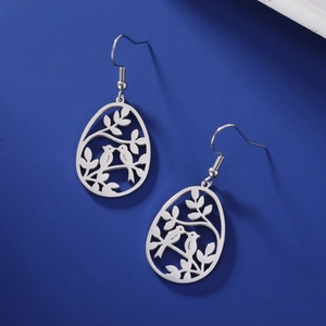 Détail de boucles d'oreilles argentées en forme d'œuf avec oiseaux sur fond bleu roi