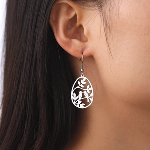 Boucles d'oreilles oiseaux en acier argenté avec motif ajouré portées par un mannequin