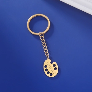 Detail showing gold artist palette keychain with paint brush on dark blue background