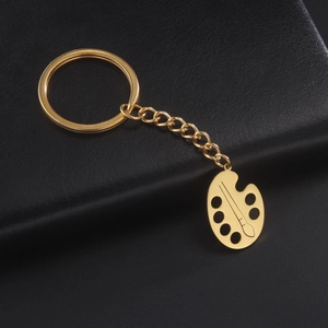 Detail of a gold palette keychain with paintbrush engraving on black leather background