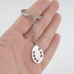 Minimalist stainless steel artist palette keychain with paint brush pendant held in hand