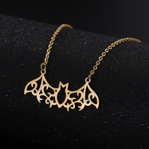 Close-up of golden bat pendant with intricate filigree patterns on black display stand