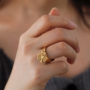Gold stainless steel band ring featuring a hanging Celtic knot clover charm for women