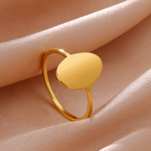 Minimalist gold oval signet ring in polished stainless steel on champagne silk background