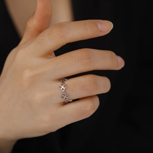 Detailed close-up of a hollow four-leaf clover pattern ring on a finger with black backdrop