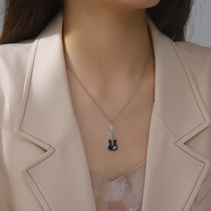 Close-up of guitar pendant necklace with black enamel and crystals on female model