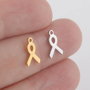 Miniature ribbon heart charms in gold and silver steel held between fingers for size