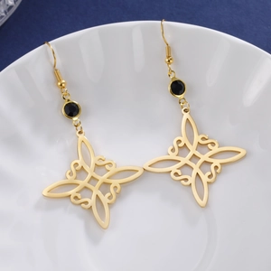 Goldene Hexenknoten-Ohrringe mit schwarzem Edelstein in einer weißen Keramikschale