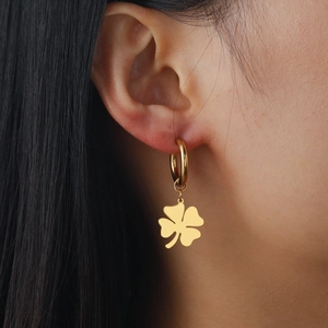 Pendientes de aro con colgante de trébol dorado pulido mostrados en una modelo real