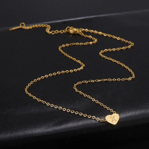 Nahaufnahme des goldenen Herzanhängers mit X-Gravur und feiner Karabiner-Halskette
