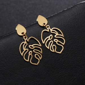 Golden monstera leaf drop earrings with hollow cutouts on black leather background