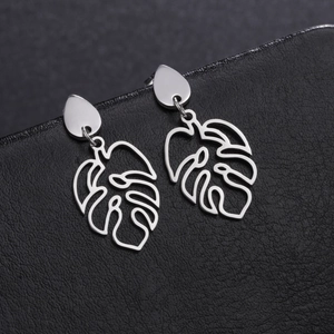 Close-up of polished stainless steel monstera leaf earrings on black leather texture