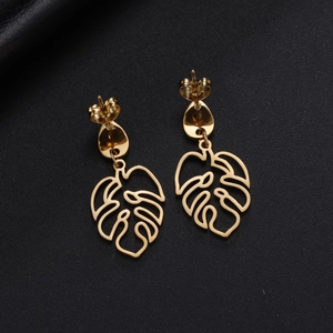 Detail view of golden hollow monstera leaf earrings with teardrop clasp on black background
