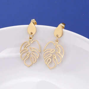 Detailed view of gold leaf drop earrings with monstera cutouts on a white bowl
