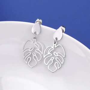 Macro detail of silver monstera leaf earrings hanging on a white ceramic plate