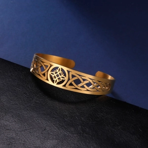 Golden stainless steel cuff bracelet featuring a hollow Celtic knot design on a dark base