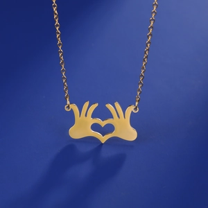 Dettaglio del ciondolo a forma di mani a cuore su collana in acciaio inossidabile dorato