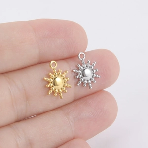 Polished stainless steel sun pendant charms in gold and silver held by hand
