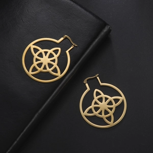 Detail of gold Celtic knot earrings with intricate cutouts on a black leather background