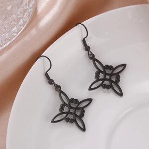 Detalle de pendientes geométricos negros mate sobre un elegante plato de cerámica blanca