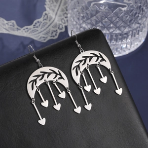 Detail of silver crescent moon earrings with leaf textures and heart tassel charms