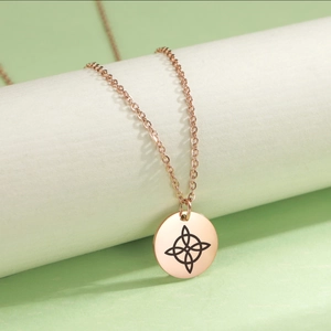 Primer plano del colgante de nudo de bruja en oro rosa sobre soporte de joyas blanco