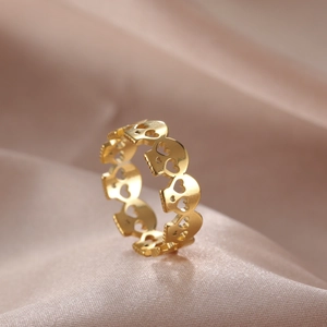 Macro detail of high-polish gold ring with hollow heart-eye skull patterns on satin