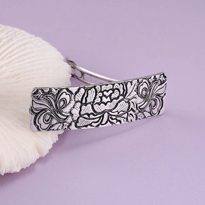 Detail of vintage silver alloy hair clip featuring embossed peony floral patterns