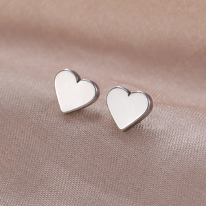 Macro shot of silver heart stud earrings resting on premium champagne pink silk fabric