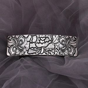 Close-up of vintage silver alloy hair clip with detailed floral relief on mesh background