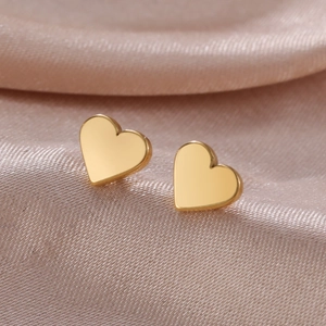 Macro shot of polished gold heart stud earrings on soft champagne satin fabric
