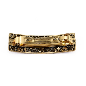 Vintage gold metal spring hair clip with embossed floral patterns on white background