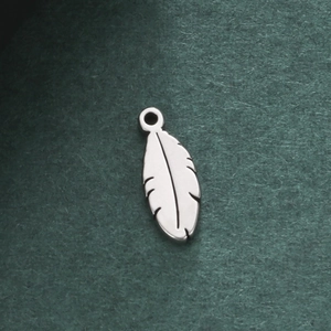 Polished stainless steel feather pendant with detailed engraving on dark green surface
