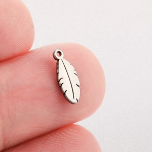 Macro shot of a tiny silver feather charm pendant in stainless steel held on a fingertip