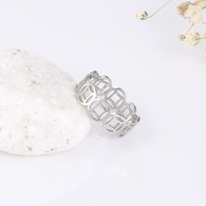 Macro shot of silver hollow coin pattern ring leaning on white stone with flowers
