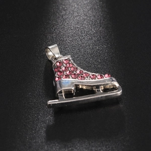 Detail view of a silver ice skate pendant with pink rhinestones on a dark textured surface