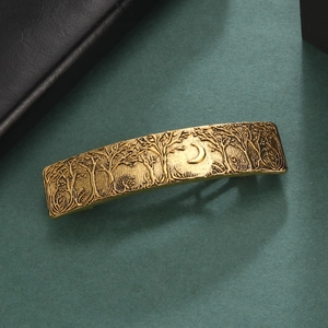 Detail of vintage gold metal hair clip with embossed forest and moon scene