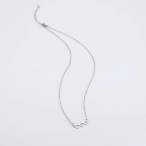 Dettaglio macro della collana in acciaio argento con pendente a tre cuori traforati