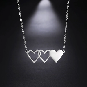 Dettaglio di tre ciondoli a cuore intrecciati su una sottile catena color argento